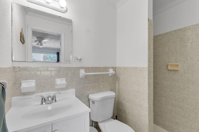 bathroom featuring a wainscoted wall, crown molding, tile walls, toilet, and vanity