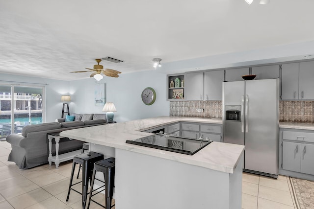 kitchen with light countertops, visible vents, open floor plan, stainless steel fridge, and black electric cooktop