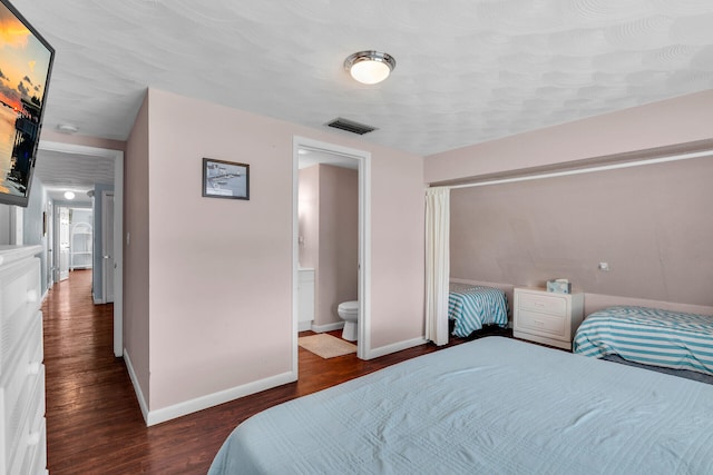 bedroom featuring ensuite bath, baseboards, visible vents, and dark wood-type flooring