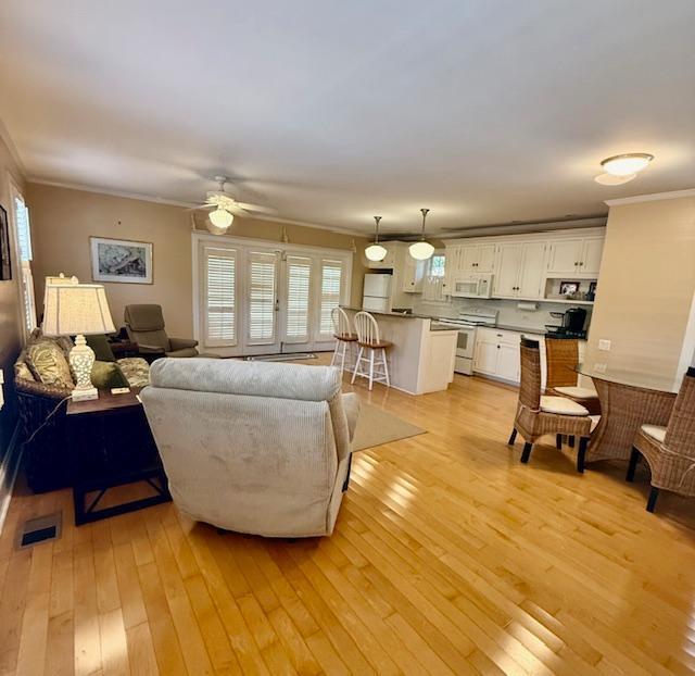 living room featuring crown molding, ceiling fan, visible vents, and light wood-style floors