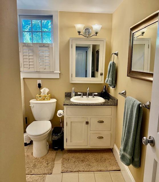 half bath featuring tile patterned floors, toilet, baseboards, and vanity
