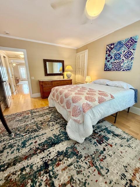 bedroom featuring ornamental molding, light wood-style floors, ceiling fan, and baseboards