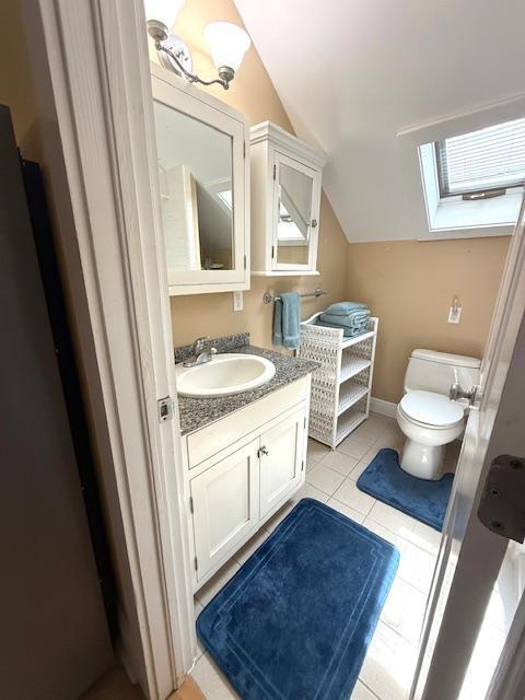 half bath with toilet, vaulted ceiling with skylight, vanity, tile patterned flooring, and baseboards