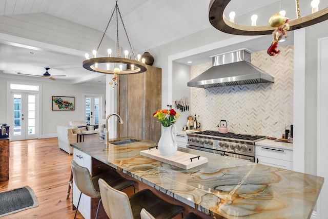 kitchen featuring wall chimney exhaust hood, double oven range, a sink, tasteful backsplash, and vaulted ceiling