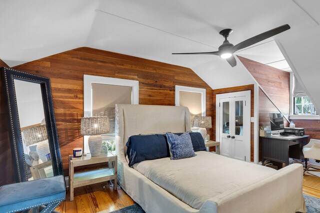 bedroom featuring vaulted ceiling, wood walls, wood finished floors, and a ceiling fan