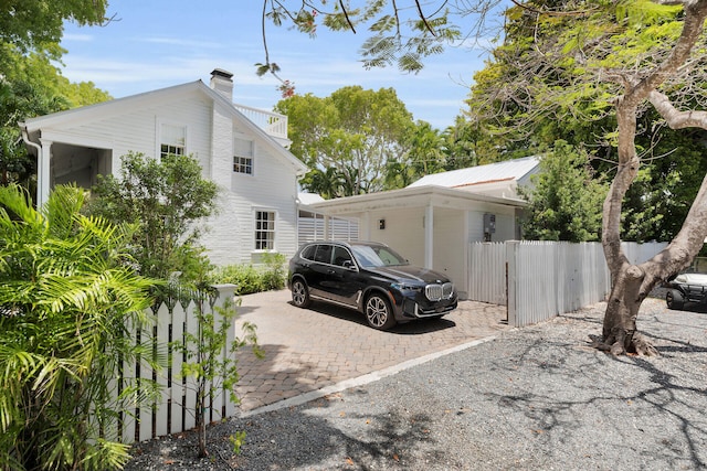 view of side of property featuring fence, driveway, a chimney, and a balcony