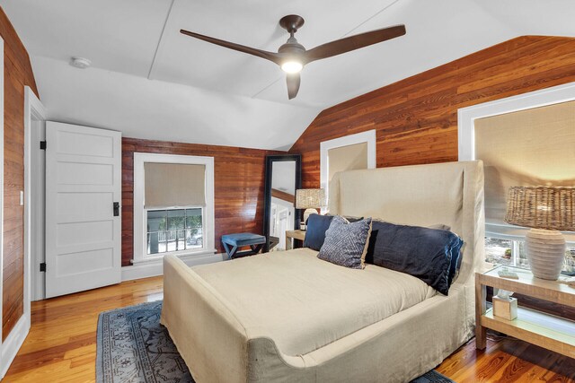 bedroom with wood walls, lofted ceiling, a ceiling fan, and light wood finished floors