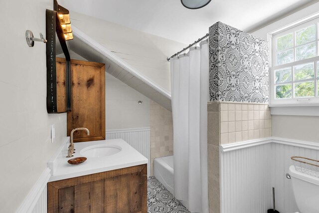 bathroom with a wainscoted wall, toilet, vanity, curtained shower, and a bathtub