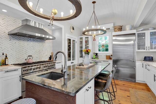 kitchen with high end appliances, wall chimney exhaust hood, a chandelier, lofted ceiling, and a sink