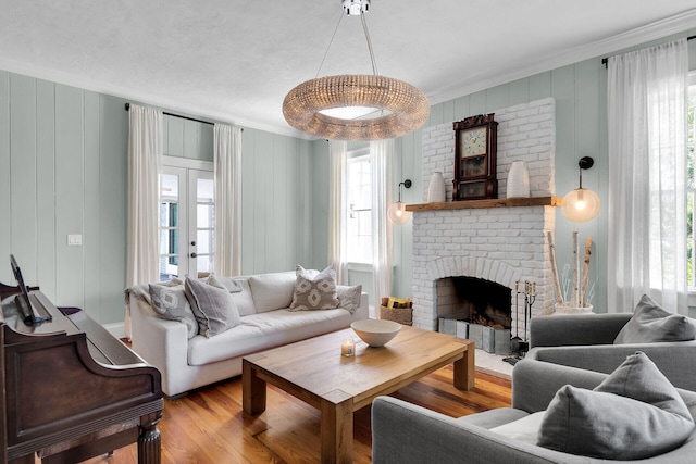 living area with ornamental molding, plenty of natural light, wood finished floors, a brick fireplace, and a decorative wall