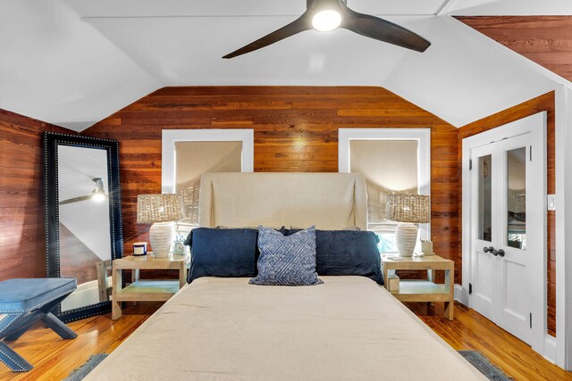 bedroom featuring wooden walls, vaulted ceiling, wood finished floors, and ceiling fan
