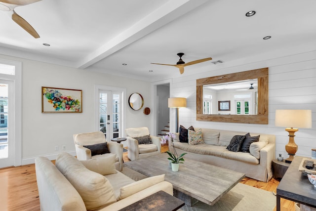 living area with a ceiling fan, healthy amount of natural light, light wood-style floors, wood walls, and beam ceiling