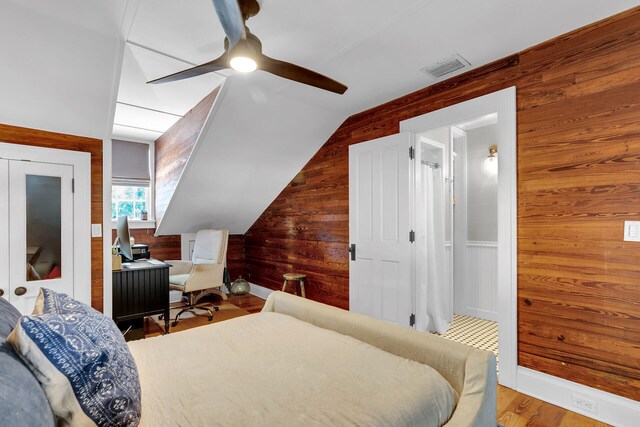 bedroom featuring wooden walls, vaulted ceiling, wood finished floors, and ceiling fan