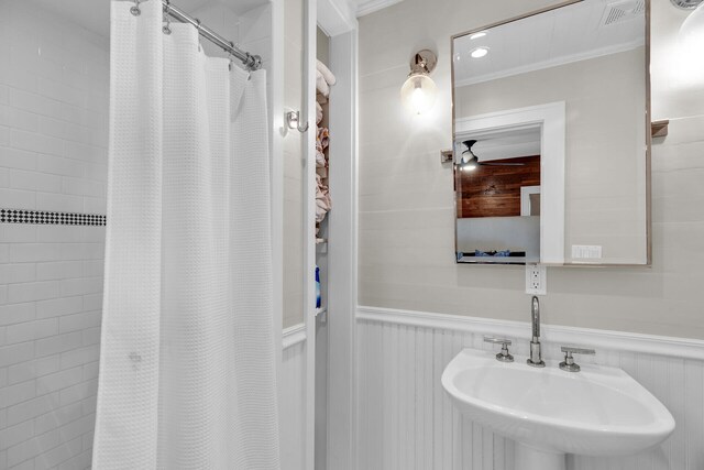 full bathroom featuring a sink, wainscoting, a shower with shower curtain, and ornamental molding