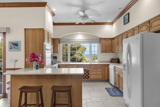 kitchen featuring crown molding, white appliances, ceiling fan, a kitchen breakfast bar, and kitchen peninsula