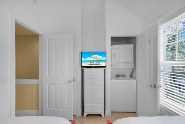 bedroom featuring stacked washer and dryer, light tile patterned flooring, and vaulted ceiling