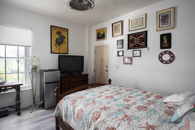 bedroom with light hardwood / wood-style flooring, stainless steel fridge, and a textured ceiling