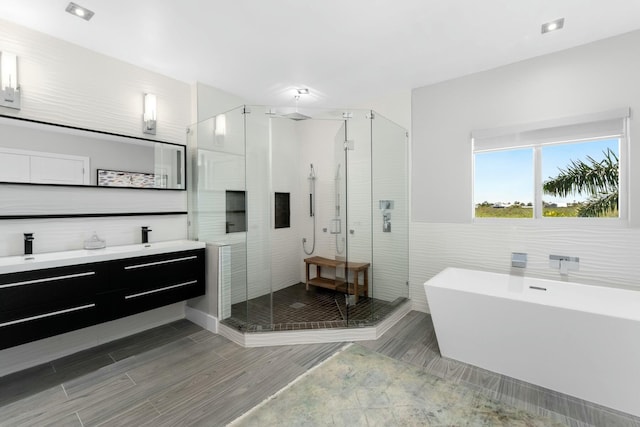 full bath featuring a freestanding bath, tile walls, vanity, a stall shower, and wood finish floors