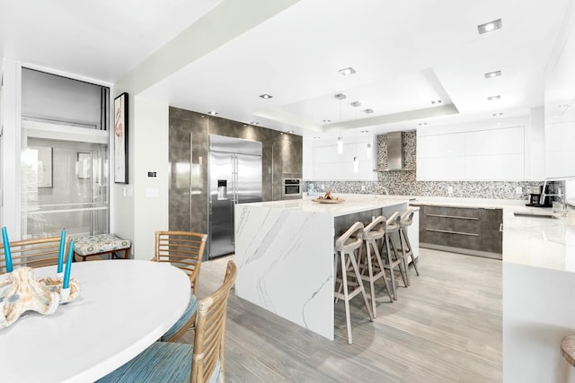 kitchen with a breakfast bar area, stainless steel built in refrigerator, a center island, modern cabinets, and a tray ceiling