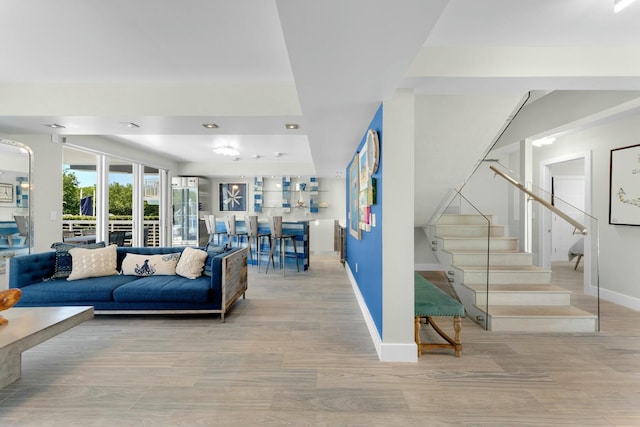 living area with stairs, light wood-style floors, and baseboards