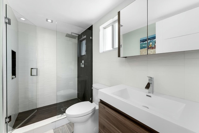 full bathroom with vanity, toilet, a stall shower, and tile walls