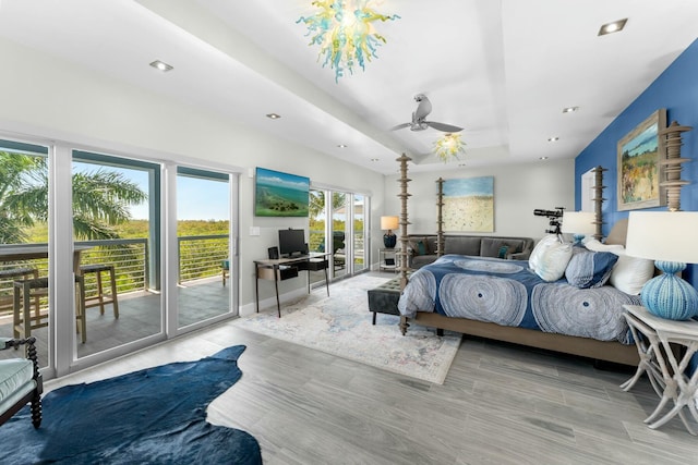 bedroom with recessed lighting, access to exterior, wood finished floors, and a tray ceiling