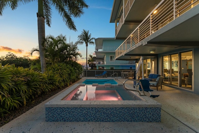 pool at dusk featuring a pool with connected hot tub and a patio area