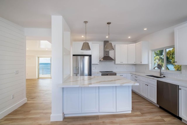 kitchen with white cabinets, wall chimney exhaust hood, light stone countertops, stainless steel appliances, and a sink