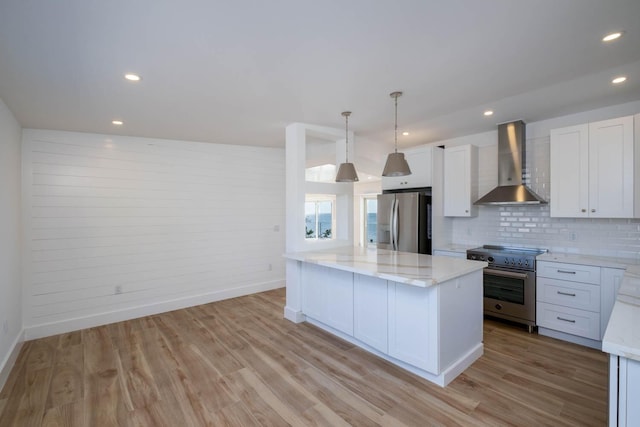 kitchen with white cabinets, wall chimney exhaust hood, stainless steel appliances, light wood-type flooring, and backsplash