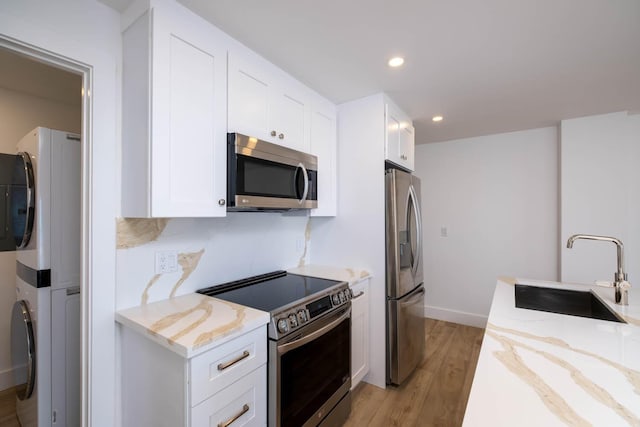 kitchen with light wood-style flooring, stainless steel appliances, stacked washer / dryer, a sink, and light stone countertops