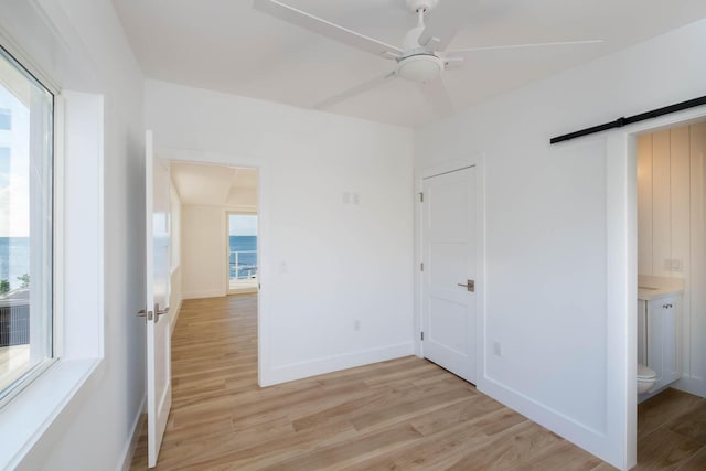 spare room with a ceiling fan, light wood-style flooring, baseboards, and a barn door