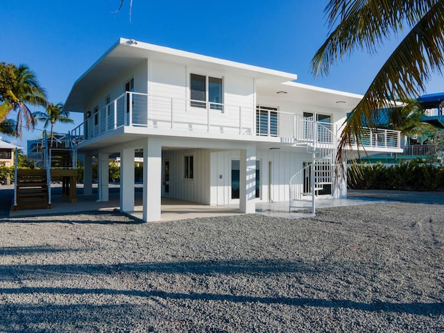 back of house featuring driveway, a patio, stairway, a carport, and board and batten siding