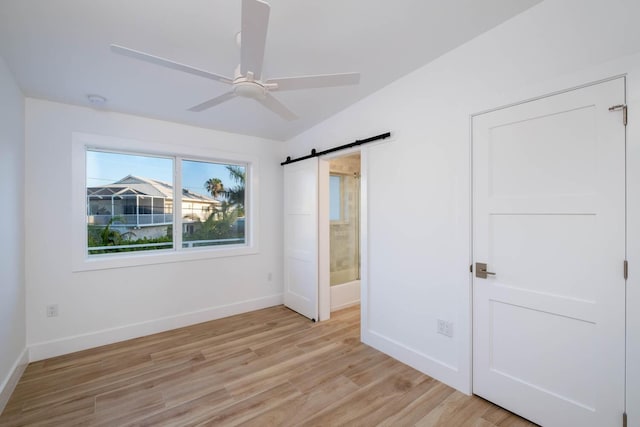 unfurnished bedroom featuring a barn door, connected bathroom, a ceiling fan, baseboards, and light wood-style floors