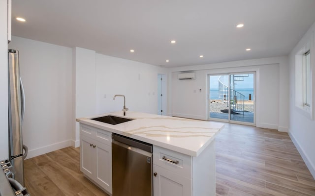 kitchen with a wall unit AC, stainless steel appliances, a sink, white cabinets, and light wood finished floors