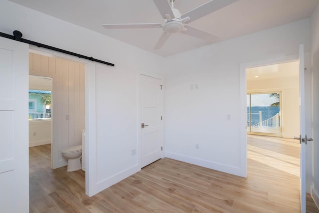 unfurnished bedroom with a barn door, multiple windows, baseboards, and light wood-style flooring