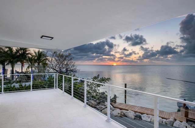 balcony at dusk featuring a water view