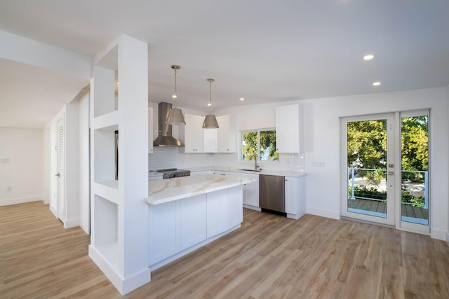 kitchen featuring a sink, light wood-style floors, white cabinets, wall chimney range hood, and stainless steel dishwasher