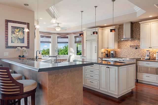 kitchen featuring dark hardwood / wood-style floors, tasteful backsplash, a breakfast bar area, a raised ceiling, and wall chimney exhaust hood