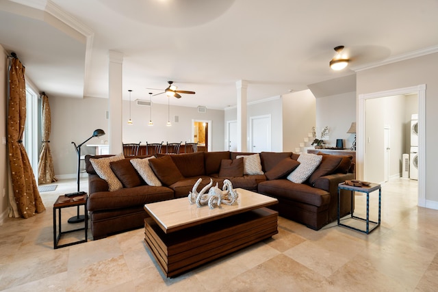 living room featuring decorative columns, stacked washing maching and dryer, ornamental molding, and ceiling fan