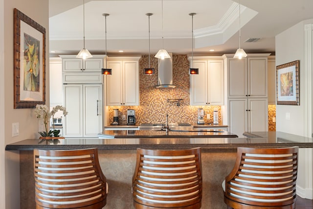 interior space with paneled built in refrigerator, hanging light fixtures, tasteful backsplash, ornamental molding, and wall chimney exhaust hood