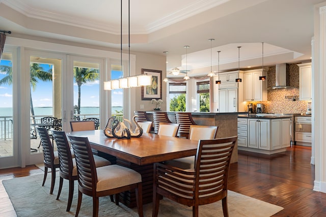 dining space featuring ornamental molding, a water view, dark hardwood / wood-style flooring, and a tray ceiling