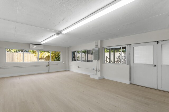 spare room featuring a healthy amount of sunlight, a wall mounted AC, electric panel, and light hardwood / wood-style floors