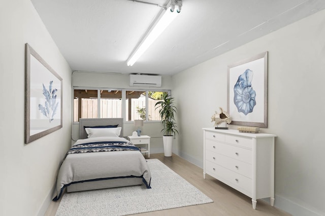 bedroom with light hardwood / wood-style floors and an AC wall unit