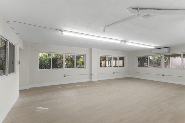 empty room featuring a healthy amount of sunlight, a wall mounted air conditioner, and light wood-type flooring