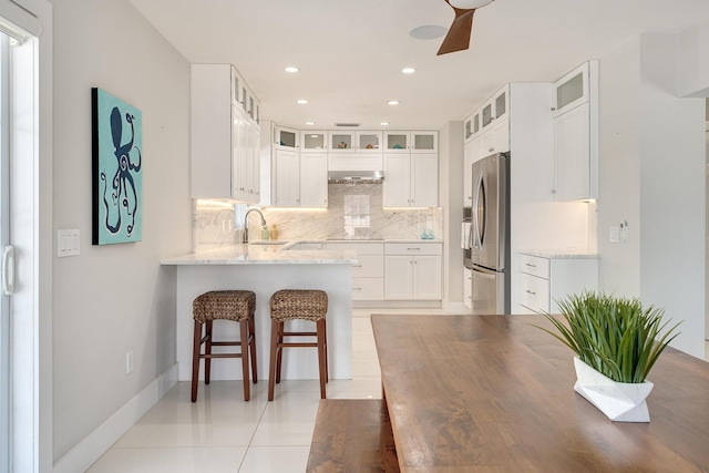 kitchen featuring stainless steel refrigerator, white cabinetry, sink, decorative backsplash, and light stone counters