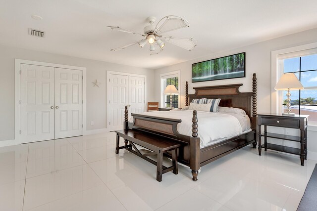 bedroom with ceiling fan, light tile patterned floors, and two closets