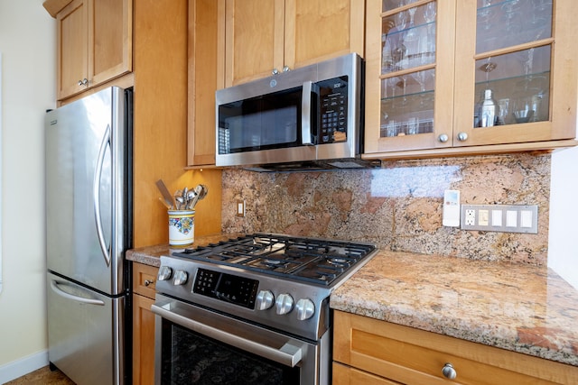 kitchen featuring light stone counters, tasteful backsplash, appliances with stainless steel finishes, glass insert cabinets, and baseboards