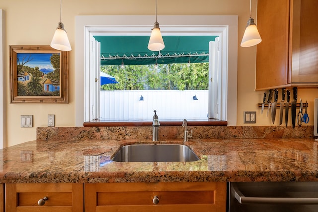 kitchen with hanging light fixtures, stone counters, brown cabinets, and a sink