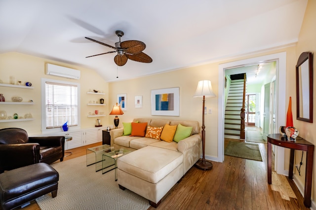 living area with baseboards, a ceiling fan, a wall unit AC, lofted ceiling, and wood finished floors