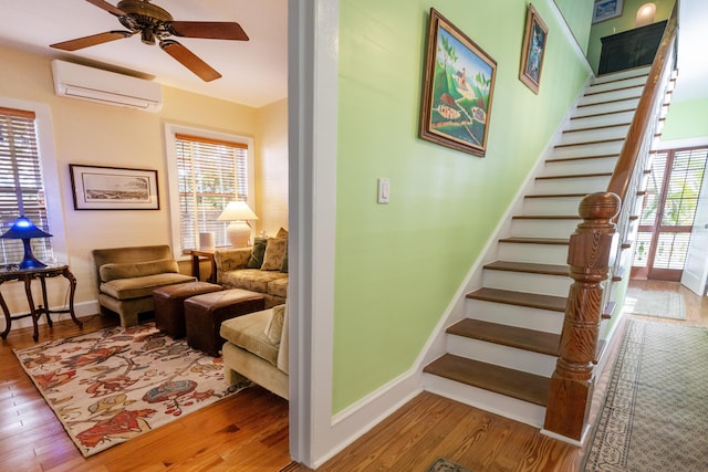 living room with stairway, a wall mounted AC, wood finished floors, and a wealth of natural light